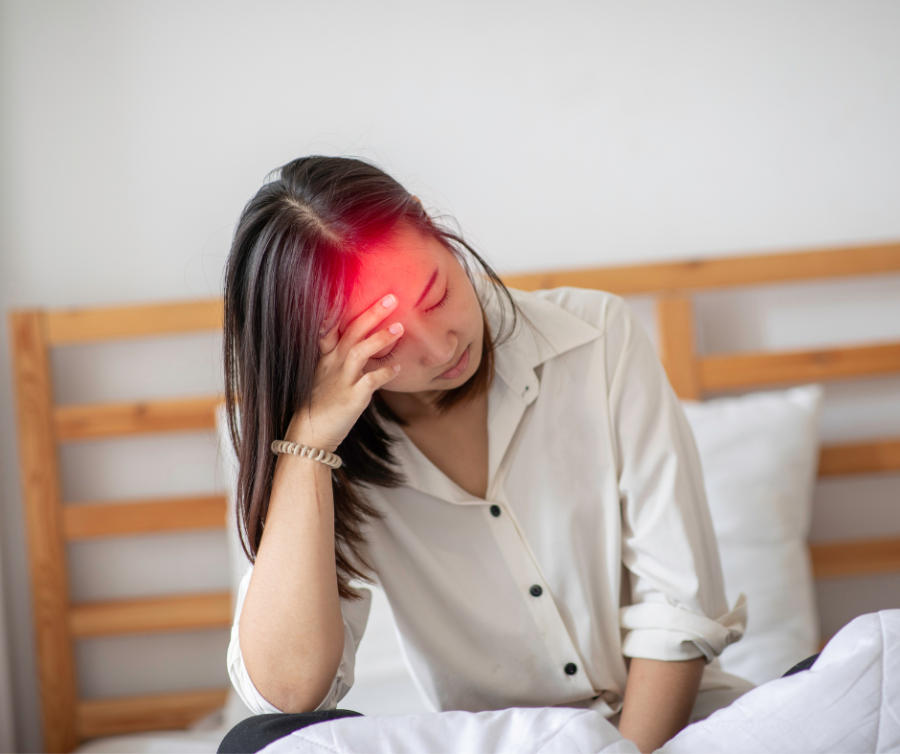Vrouw met hormonale migraine door spiraal zit op bed met hoofdpijnklachten